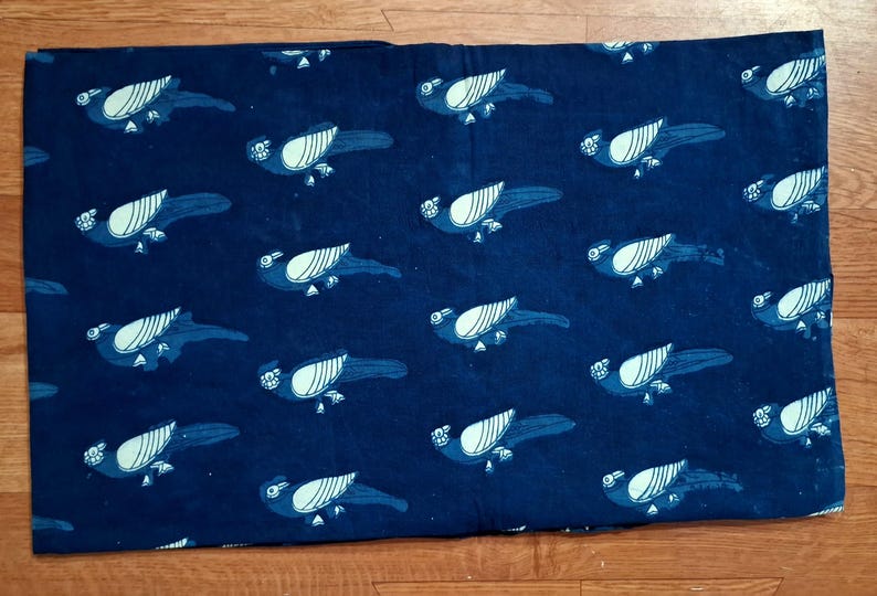 May include: A rectangular piece of dark blue fabric featuring a repeating pattern of stylised birds in a lighter blue shade. Each bird is depicted in profile with a distinct wing design and a small head, arranged in a consistent grid across the textile.