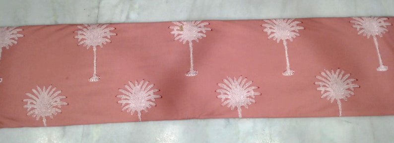 May include: A coral-colored fabric with a repeating pattern of white palm trees. The palm trees are embroidered with detailed fronds and trunks. The fabric is likely used for home decor or apparel.