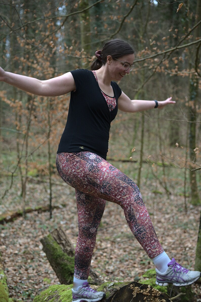 May include: A woman wearing a black shirt and patterned leggings is balancing on a tree trunk in a forest. She is wearing purple and white sneakers.