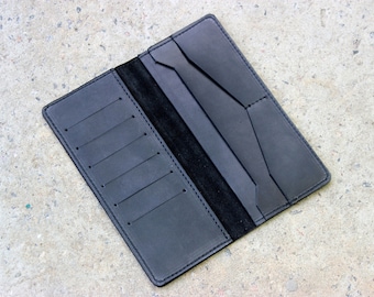 May include: A black leather wallet with multiple card slots and a billfold. The wallet is open and laid flat on a gray concrete surface.