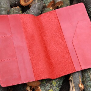 Puede incluir: Carpeta de cuero roja para cuaderno con varios bolsillos y cierre de solapa. La carpeta est&aacute; abierta para revelar un interior de ante rojo.