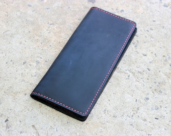 May include: A black leather wallet with red stitching. The wallet is closed and lying flat on a concrete surface.