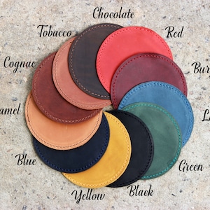 Puede incluir: Una variedad de posavasos de cuero en diferentes colores, incluyendo negro, marr&oacute;n, rojo, azul, verde, amarillo y caramelo. Los posavasos est&aacute;n dispuestos en un c&iacute;rculo con los nombres de los colores escritos encima de cada posavasos.