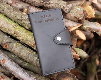 May include: Black leather wallet with a flap closure and a silver button. The wallet has the text "M.J.C.S I AM (UN)WILLING" engraved on the front.