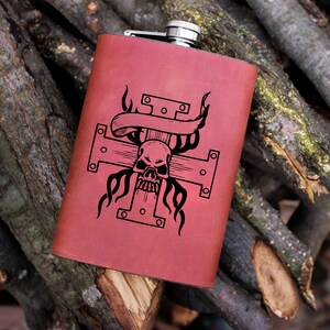 May include: A red leather-wrapped flask with a skull and crossbones design. The design features a skull with flames and a banner.