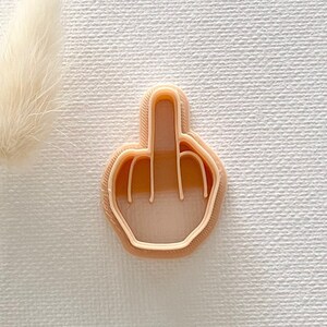 May include: A light brown plastic cookie cutter shaped like a hand giving the middle finger.