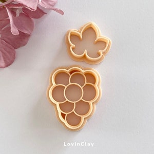 May include: Two tan polymer clay cutters, one a leaf shape, the other a bunch of grapes. The grape cutter has individual grape shapes. The leaf cutter is a simple five-lobed design. The text "LovinClay" is at the bottom of the image.