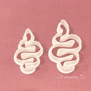 May include: Two white plastic cookie cutters shaped like a snake in a curled position. The cutters are on a pink background.