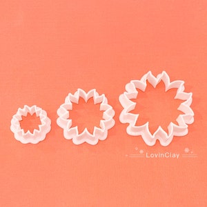 May include: Three white plastic cookie cutters shaped like flowers with different sizes. The largest cutter has 12 points, the middle cutter has 10 points, and the smallest cutter has 8 points.