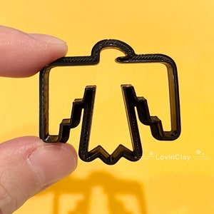 May include: Black plastic cookie cutter shaped like a stylised bird with a rounded head and wings. The cutter has a detailed design with a textured surface.