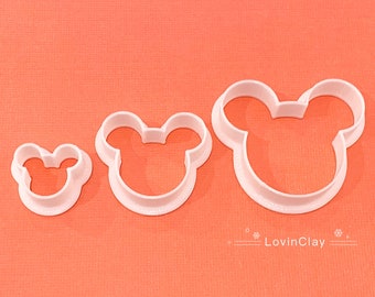 May include: Three white plastic cookie cutters shaped like a cartoon mouse head with large ears. The cutters are arranged in a row from smallest to largest.