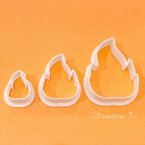 May include: Three white plastic cookie cutters shaped like flames. The cutters are different sizes, with the largest cutter at the top of the image and the smallest cutter at the bottom.
