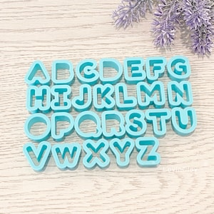 May include: A set of 26 blue plastic alphabet cookie cutters. The cutters are arranged in alphabetical order.