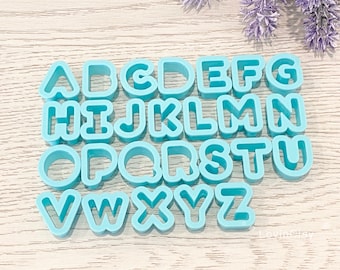 May include: A set of 26 blue plastic alphabet cookie cutters. The cutters are arranged in alphabetical order.