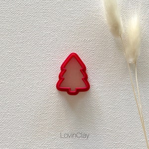 May include: A bright pink plastic Christmas tree cookie cutter. The cutter has a simple design with a rounded top and a pointed bottom.