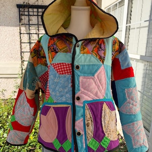 May include: A hooded jacket constructed from a patchwork of multicolored fabric squares, including red, blue, purple, pink, and orange patterns. The garment features a front button closure, a yellow-lined hood, and black trim along the edges.
