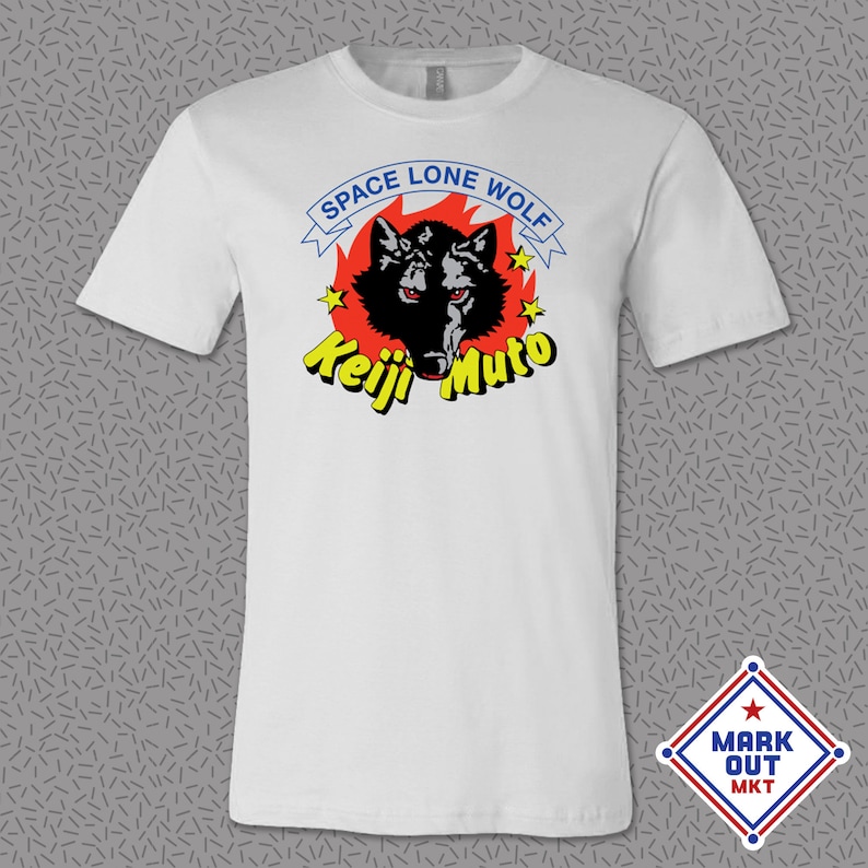 May include: White t-shirt featuring a black wolf head graphic set within a red flame. The text "Space Lone Wolf" is above the wolf and "Keiji Muto" is below the wolf.
