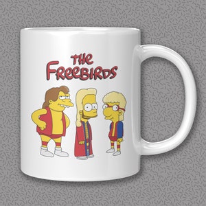 May include: White ceramic coffee mug with a cartoon image of three yellow characters with red, blue, and yellow clothing. The text "The Freebirds" is printed in black on the mug.