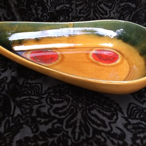 May include: A large, oval-shaped ceramic serving dish with a glossy glaze. The dish is a deep brown color with two red circles on the inside. The rim of the dish is a dark green color.