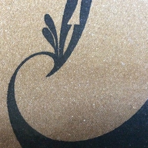 May include: A close-up of a brown textured surface with a black design of a stylized bird with a long tail and a curved neck.