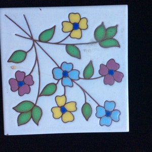 Peut inclure: Un carreau de céramique blanc avec un motif floral. Le carreau présente cinq fleurs dans des tons de jaune, bleu et rose, avec des feuilles vertes. Les fleurs sont soulignées de brun.