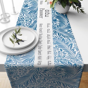 May include: A blue and white table runner with a floral pattern and Hebrew text that reads "Maza Passover Maror Korech Shulchan Orech Tzafun Barech Hall Nitza" and "צה פֶּסַח מָרוֹר כּוֹרֵךְ שָׁלְחַן עוֹרֵךְ צָפוּן בָּרֵךְ הַלֵּל נִרְצָה".
