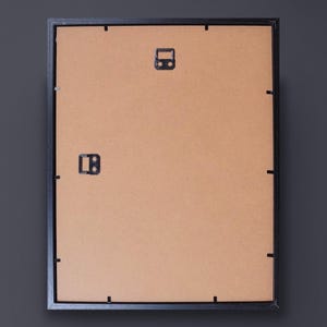 Op de afbeelding: Zwarte fotolijst met een bruine kartonnen achterkant. De lijst heeft twee metalen ophanghaken aan de achterkant.