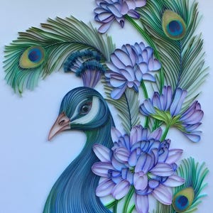 Op de afbeelding: Een pauw gemaakt van papierquilling met blauwe en groene veren. De pauw is omringd door paarse bloemen met groene stelen.