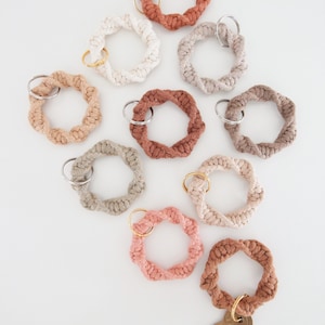May include: A set of nine crocheted keyrings in various shades of brown, beige, and pink. Each keyring features a twisted rope design and a gold metal ring.