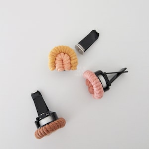 May include: Three car air fresheners with a black plastic clip and a woven rope design. The rope is in shades of pink, orange, and yellow.