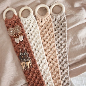 Könnte beinhalten: Vier Makramee-Wandorganizer in Braun, Beige, Creme und Grau mit Holzringen oben. Die Organizer hängen an einem beigefarbenen Stoffhintergrund und haben Ohrringe, die daran hängen.