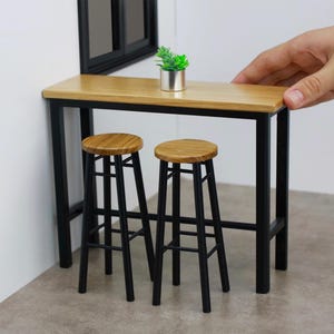Könnte beinhalten: Ein schwarzer Metall-Stehtisch mit einer Holzplatte und zwei schwarzen Metallhockern. Eine kleine Topfpflanze steht auf dem Tisch.