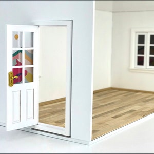 K&ouml;nnte beinhalten: Ein wei&szlig;er Puppenhausraum mit einer wei&szlig;en T&uuml;r, die ein farbenfrohes geometrisches Muster auf den Glasscheiben hat. Der Raum hat einen Holzboden und ein wei&szlig;es Fenster mit zwei Fensterscheiben.
