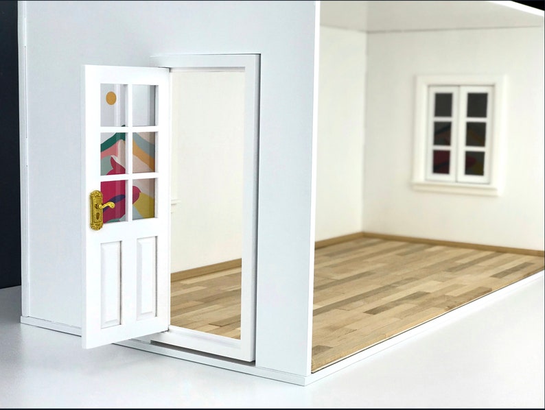 K&ouml;nnte beinhalten: Ein wei&szlig;er Puppenhausraum mit einer wei&szlig;en T&uuml;r, die ein farbenfrohes geometrisches Muster auf den Glasscheiben hat. Der Raum hat einen Holzboden und ein wei&szlig;es Fenster mit zwei Fensterscheiben.