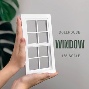 Op de afbeelding: Een wit poppenhuisraam met zes ruiten, gehouden voor een grijze achtergrond. De tekst "DOLLHOUSE WINDOW 1/6 SCALE" staat rechts van het raam.