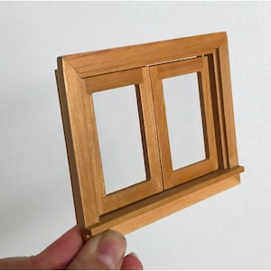 May include: A miniature wooden window frame with two panes of glass. The window frame is made of light brown wood and has a small ledge underneath.