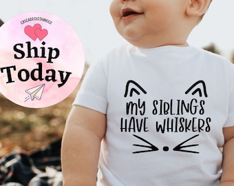 May include: White baby onesie with black text that reads "My siblings have whiskers" and a black cat face with whiskers.
