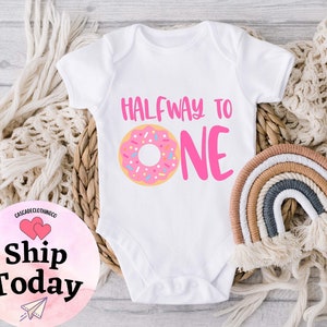 May include: White baby onesie with pink text that reads "Halfway to One" and a pink and brown donut graphic.