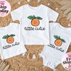 May include: Three white t-shirts with a cute orange graphic and the text "little cutie" printed on them.