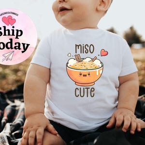May include: White baby onesie with a cartoon illustration of a bowl of miso ramen with the text "miso cute".