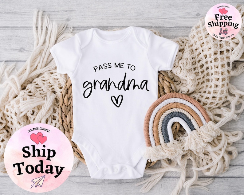 May include: White baby onesie with black text that reads "Pass me to grandma" with a small heart. The onesie is on a white background with a woven basket and a rainbow.