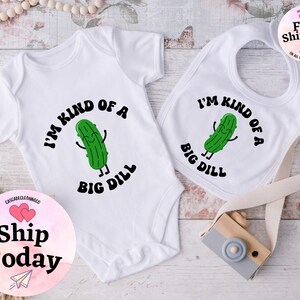 May include: A white baby bodysuit and bib with a green pickle cartoon character and the text "I'm kind of a big dill".