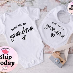 May include: White baby bodysuit and bib with black text that reads "Pass me to grandma" with a heart symbol.