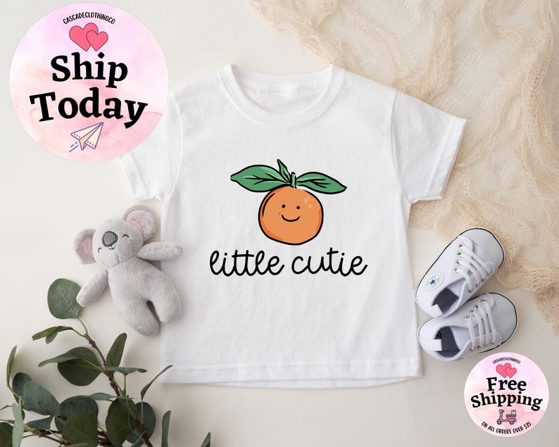 May include: White baby onesie with a smiling orange and the text "little cutie" printed on it.
