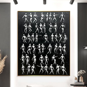May include: Large abstract painting with a black background and numerous white figures in various poses. The artwork is framed in gold and hangs on a white wall, adding a modern touch to the room's decor.