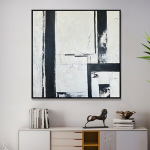May include: A square abstract painting featuring bold black vertical and horizontal lines against a textured white and light gray background, enclosed in a thin black frame. The artwork displays a high-contrast composition with visible brushstrokes.