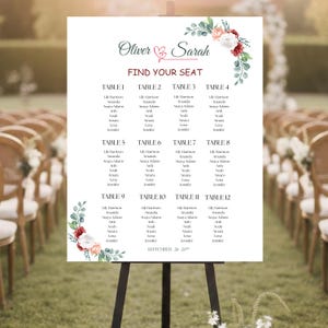 May include: A white wedding seating chart on an easel. The chart features the names "Oliver & Sarah" and "Find Your Seat" in elegant script. Floral accents in red, peach, and green adorn the corners. The chart lists guest names by table number.