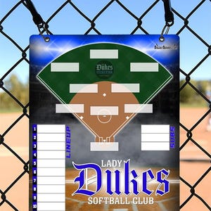 May include: A rectangular softball lineup board with a baseball field diagram, the words "Lady Dukes Softball Club," and a space for team lineups. The board is blue, green, and brown, with a chain-link fence in the background.