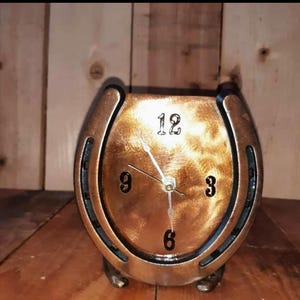 May include: A gold-colored horseshoe clock with black accents and Roman numeral markings. The clock hands are pointing to 12:00.