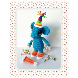 May include: A blue crocheted mouse wearing a rainbow party hat and orange shoes. The mouse is holding a small orange crocheted carrot.